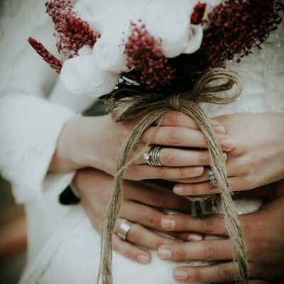 A close-up of a bride holding a rustic bouquet with groom's hands wrapped around her waist.