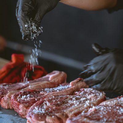 A chef seasons raw steaks with sea salt, perfecting the preparation process.